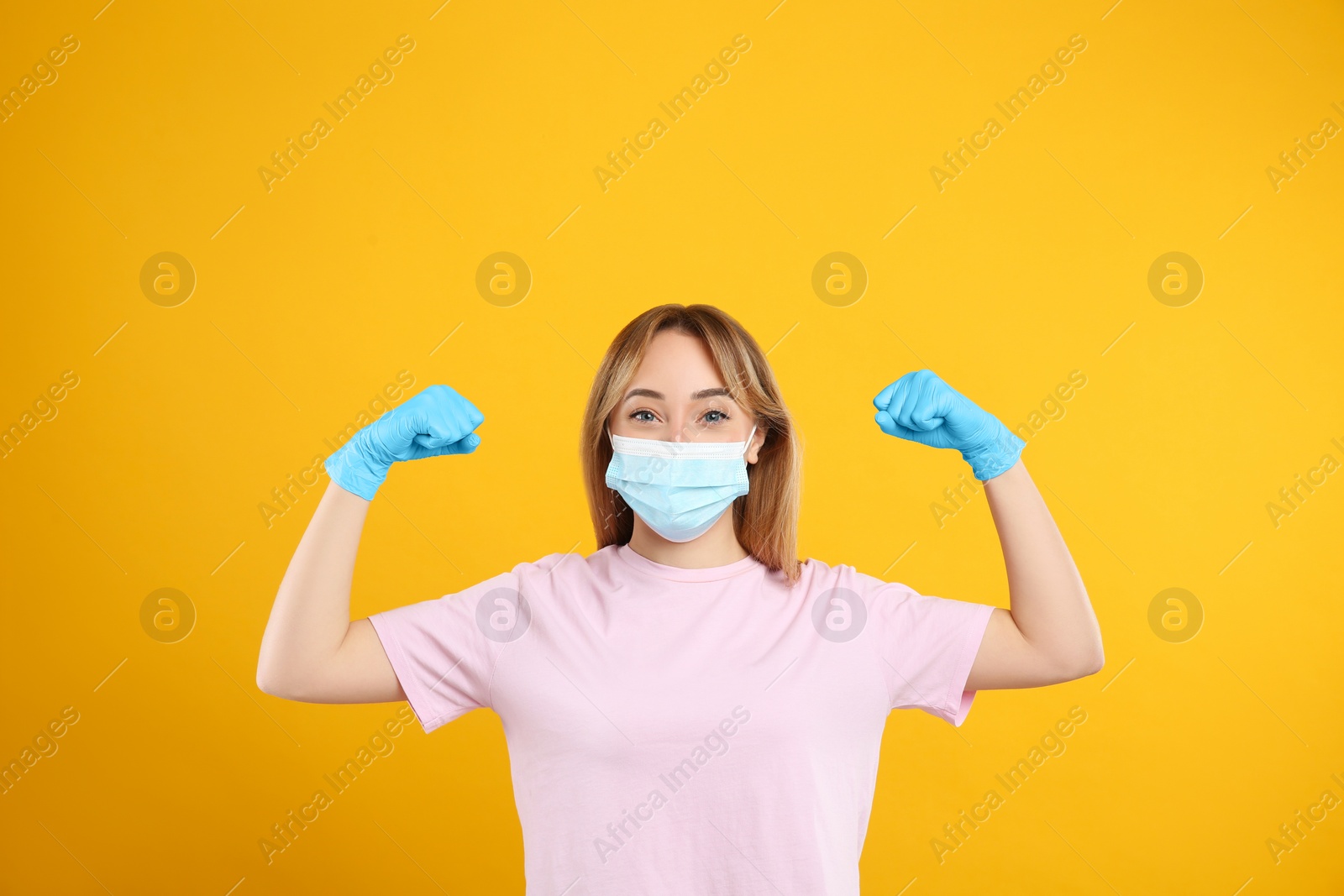 Photo of Woman with protective mask and gloves showing muscles on yellow background. Strong immunity concept