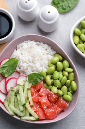 Photo of Poke bowl with salmon, edamame beans and vegetables on light grey table, flat lay
