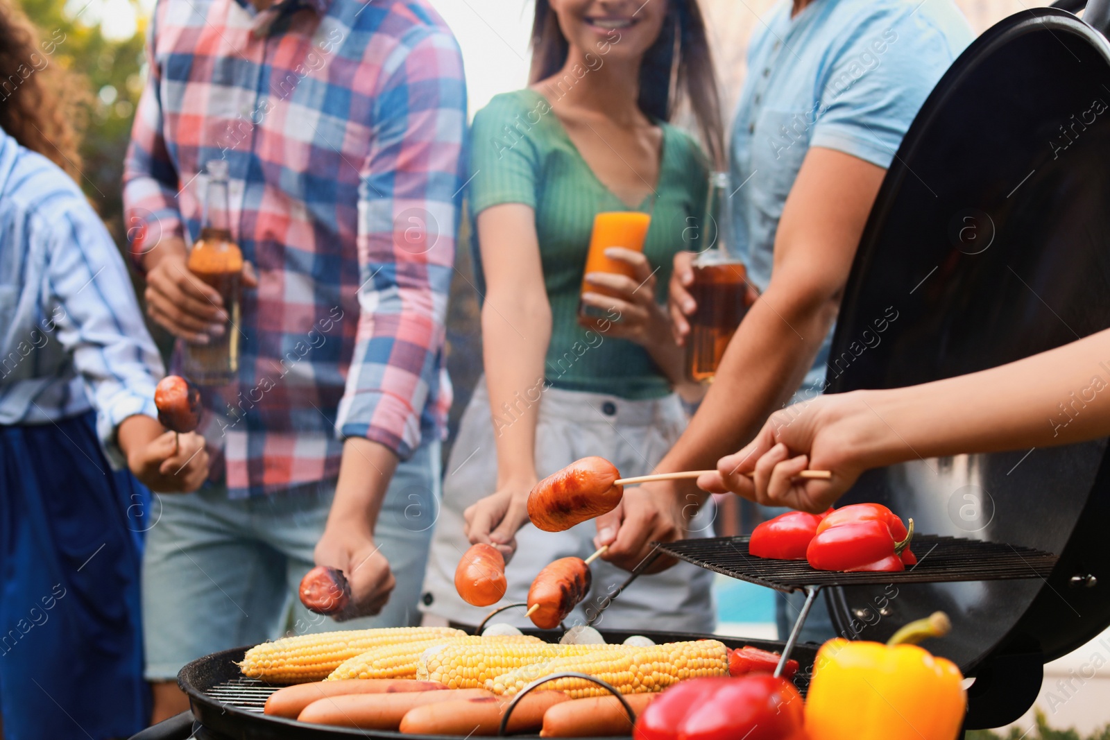 Photo of Group of friends with grilled sausages at barbecue party outdoors