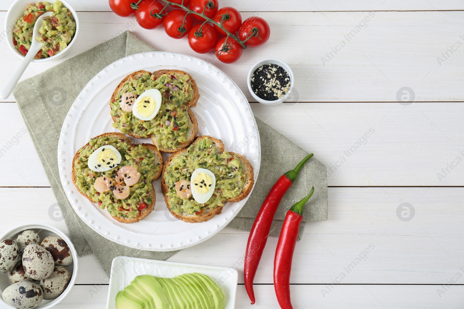 Photo of Slices of bread with tasty guacamole, eggs, shrimp and ingredients on white wooden table, flat lay. Space for text