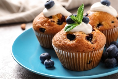 Photo of Plate of tasty muffins and blueberries on marble table, closeup