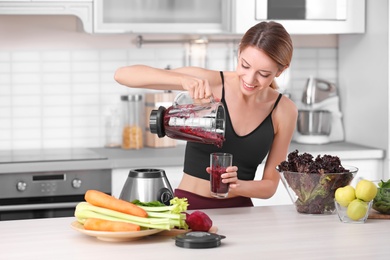 Photo of Young woman pouring tasty healthy smoothie into glass at table in kitchen