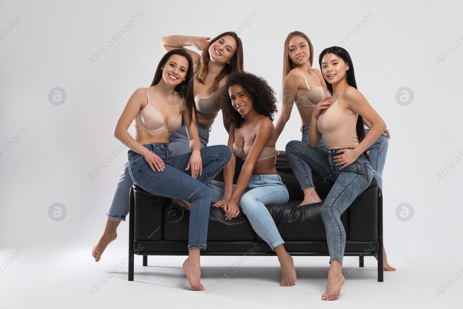 Photo of Group of women with different body types in jeans and underwear on sofa against light background