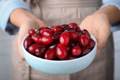 Photo of Woman with bowl of fresh ripe dogwood berries on light background, closeup