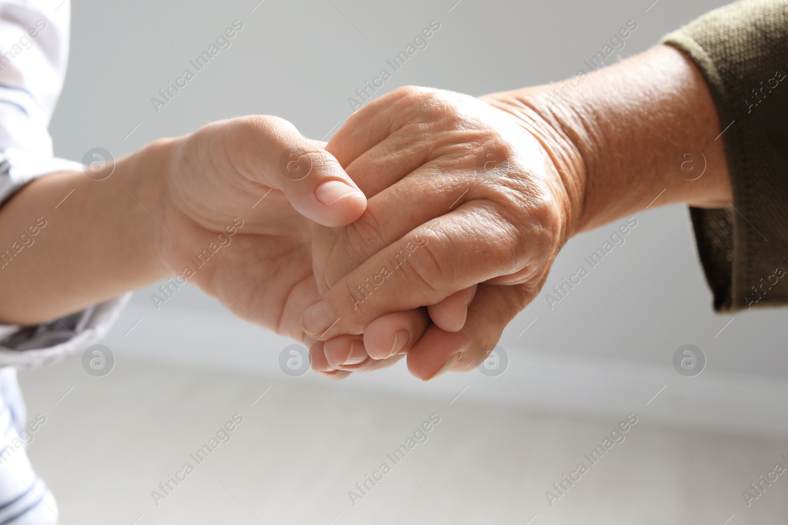 Photo of Helping hands on grey background, closeup. Elderly care concept