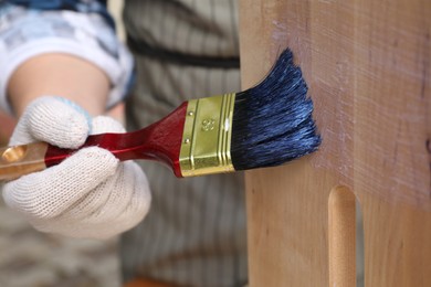 Photo of Man varnishing wooden step stool against blurred background, closeup