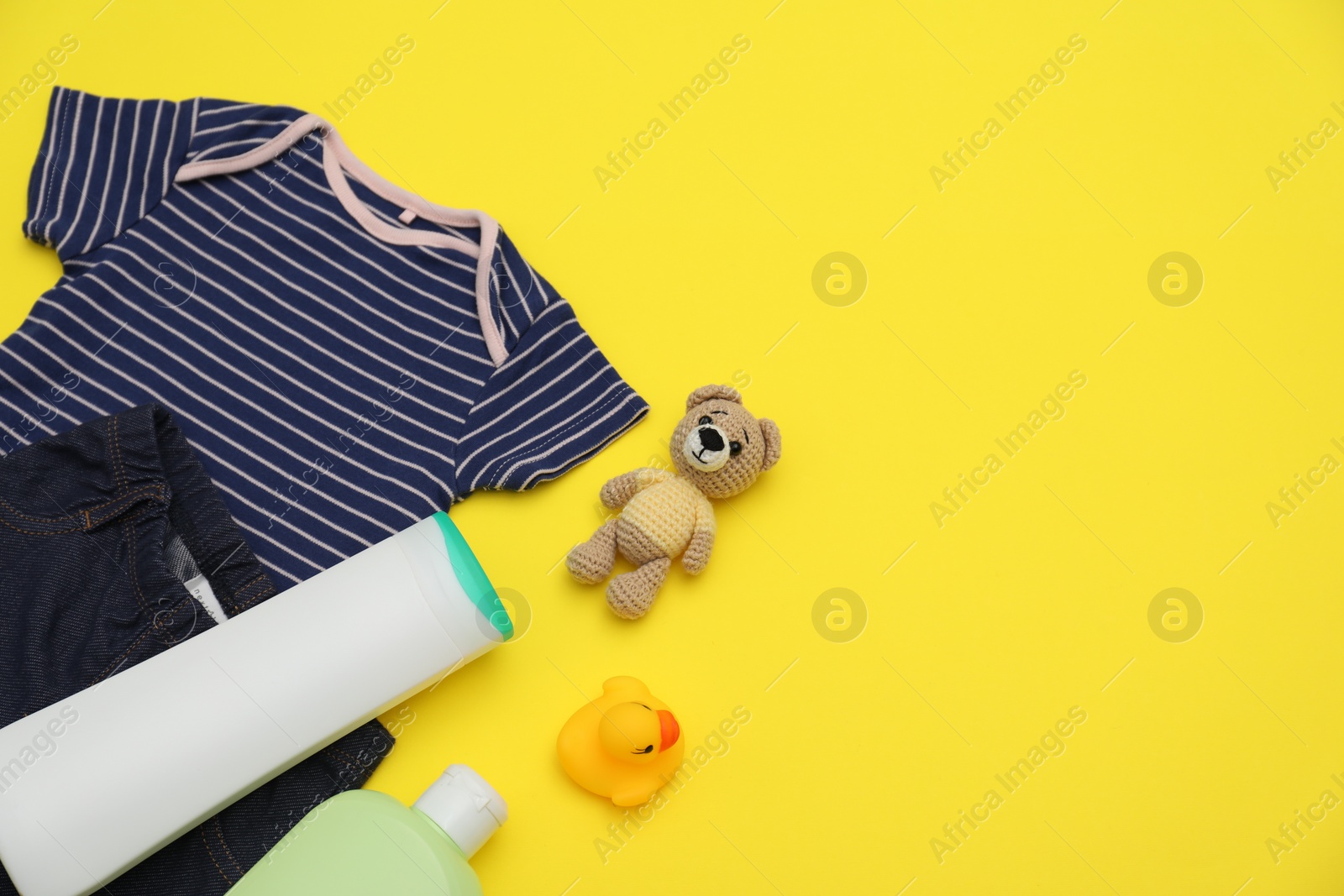 Photo of Bottles of laundry detergents, baby clothes and toy bear on yellow background, flat lay. Space for text