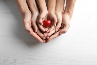 Family holding small red heart in hands on wooden background