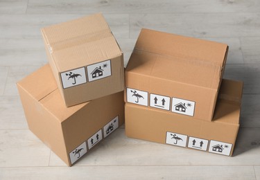 Photo of Many closed cardboard boxes with packaging symbols on wooden floor. Delivery service