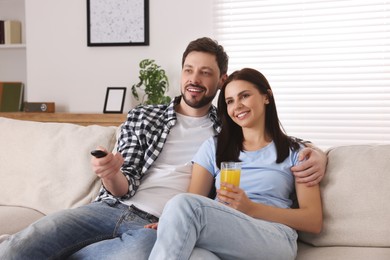 Photo of Happy couple watching show at home. Man changing TV channels with remote control