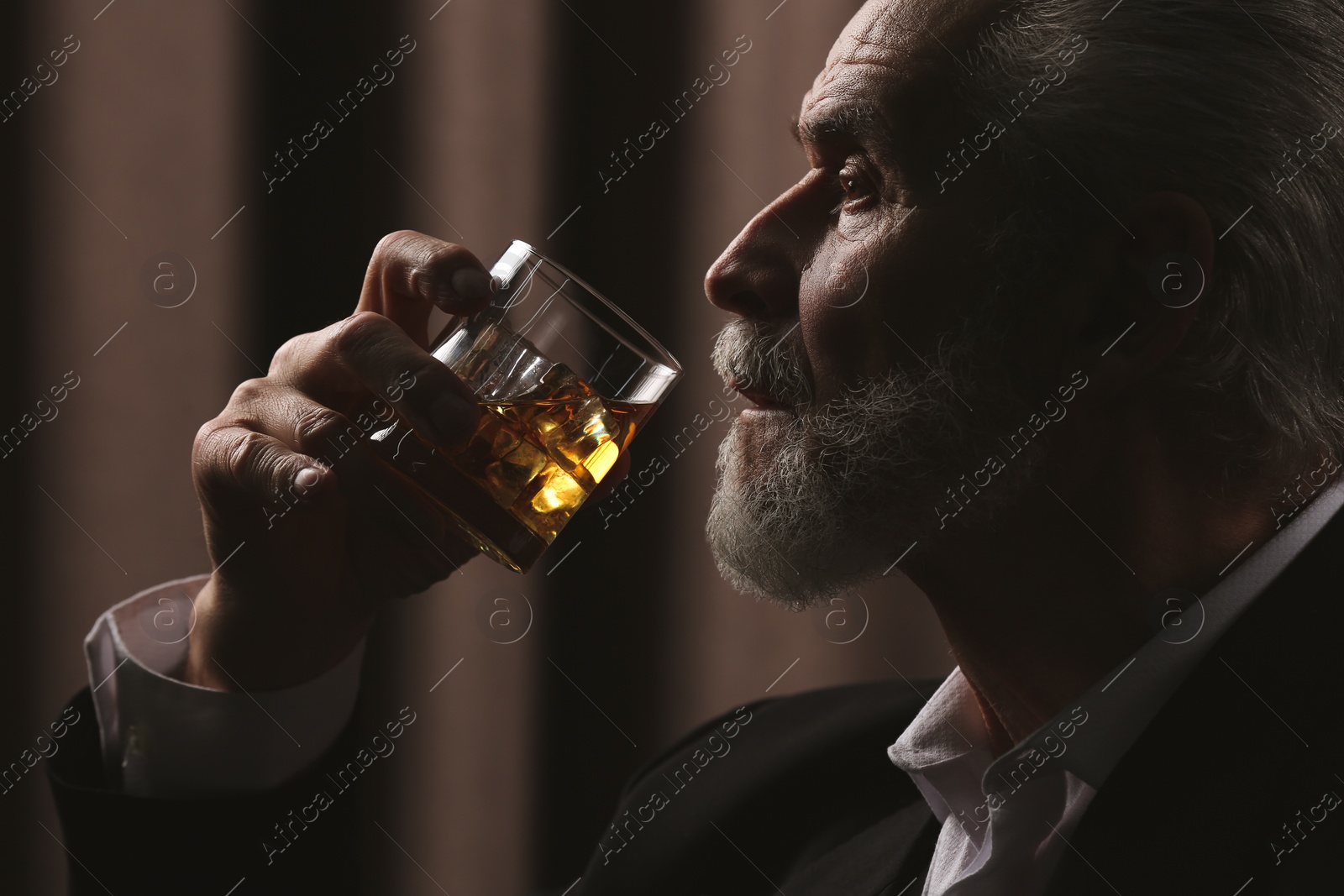 Photo of Senior man in suit drinking whiskey on brown background