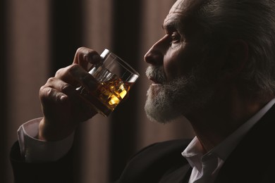 Photo of Senior man in suit drinking whiskey on brown background