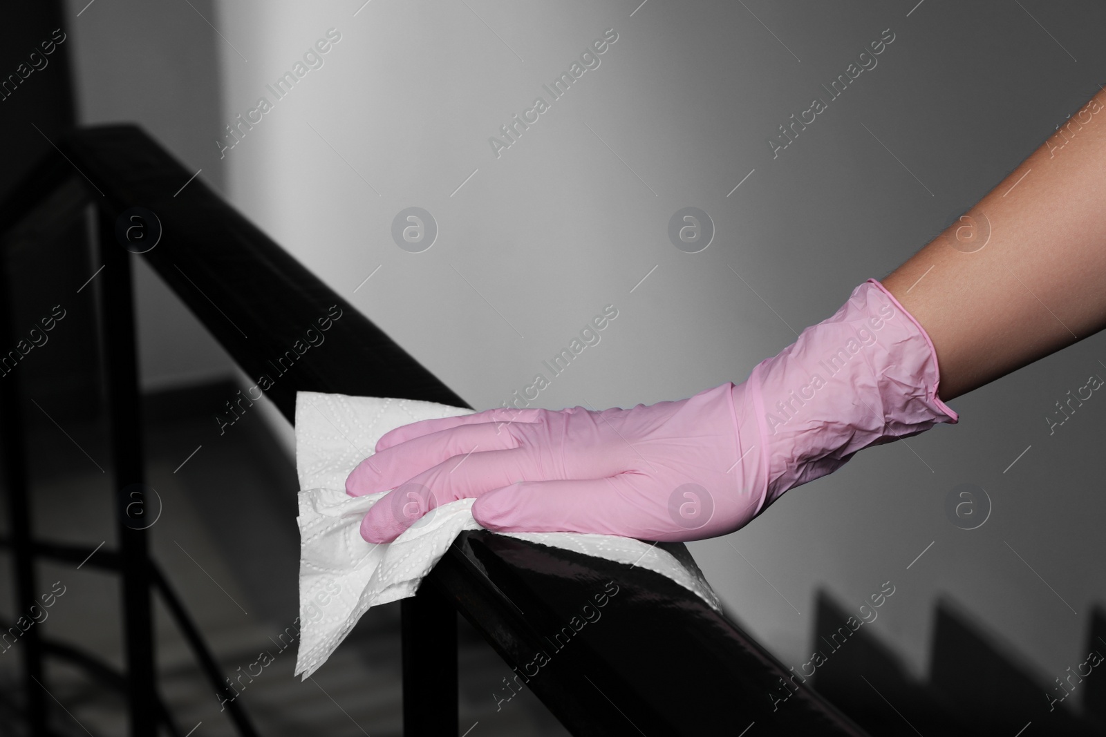 Photo of Woman in glove cleaning railing with paper towel indoors, closeup