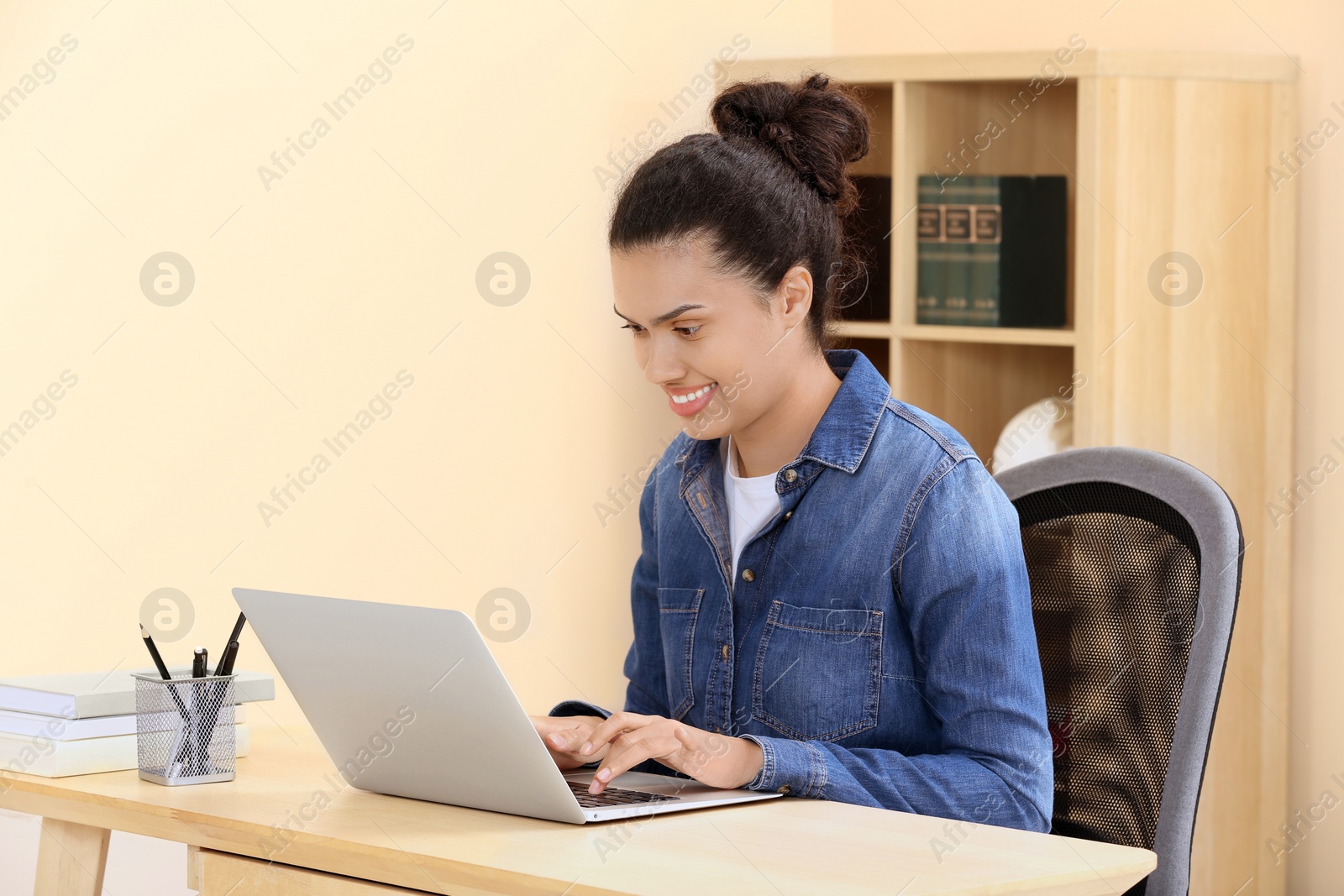 Photo of African American woman typing on laptop at wooden table indoors