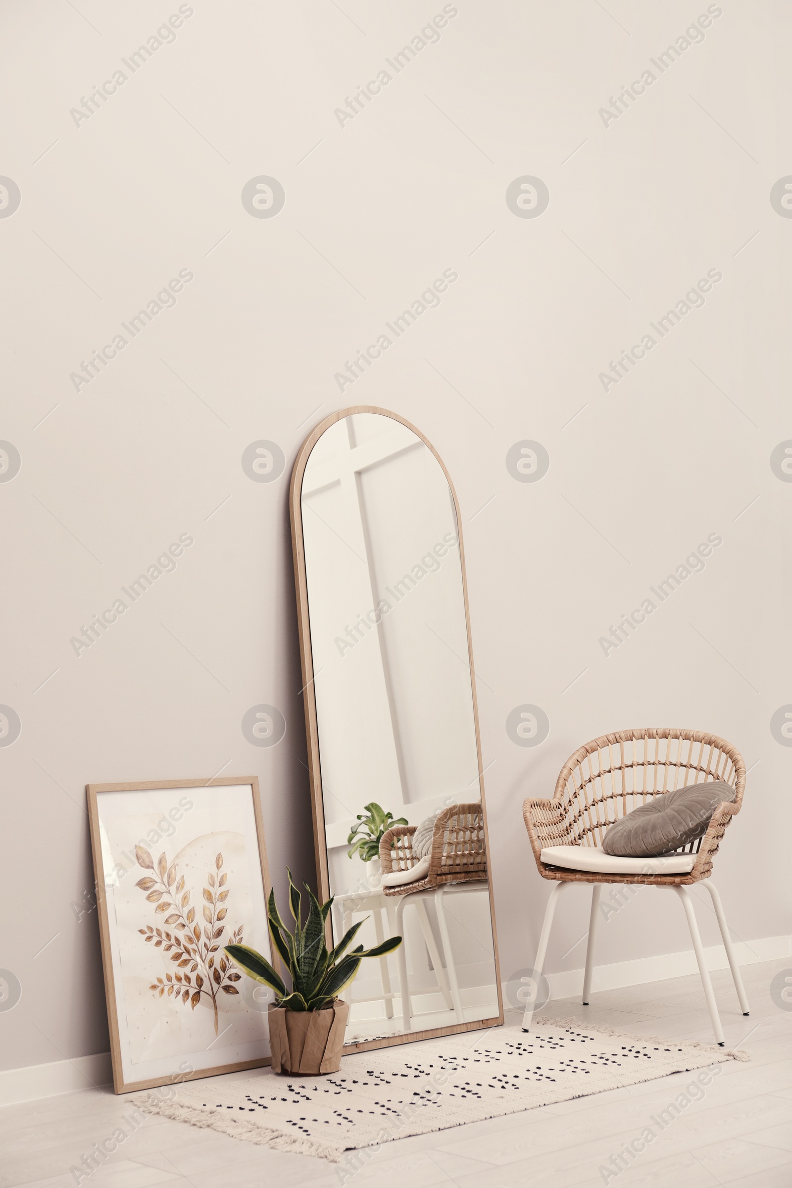 Photo of Beautiful mirror, armchair and plant near white wall indoors. Interior design