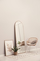 Beautiful mirror, armchair and plant near white wall indoors. Interior design