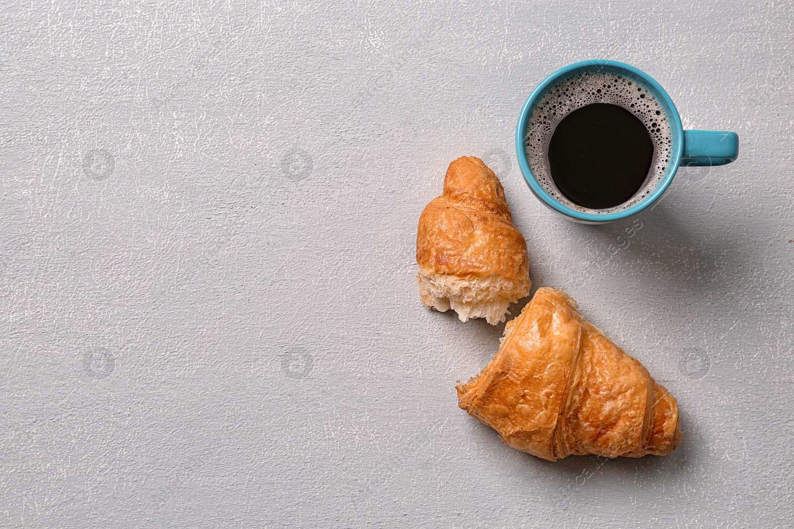 Photo of Tasty croissant and cup of coffee on light background, top view