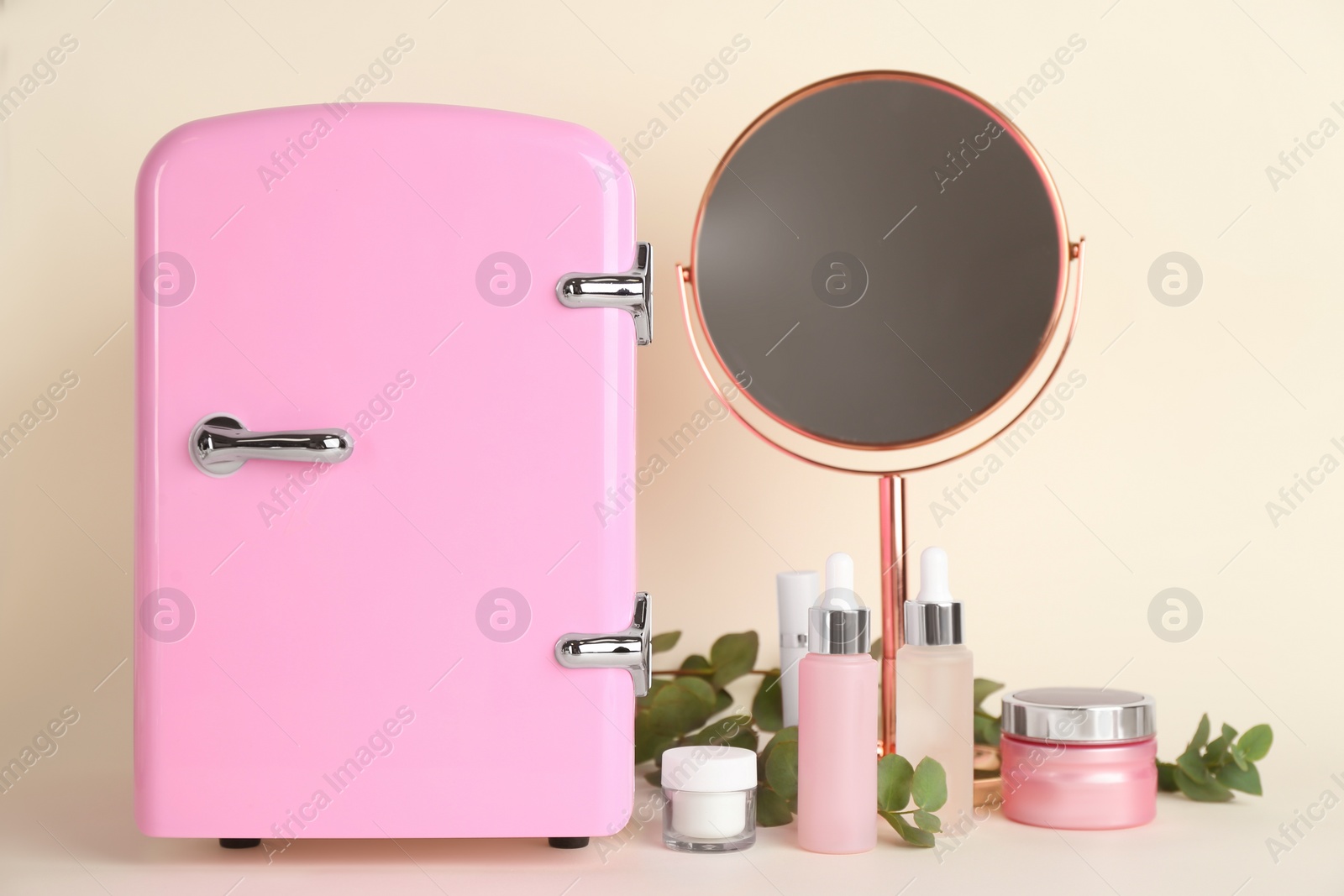 Photo of Cosmetic refrigerator and skin care products on beige background