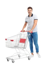 Young man with empty shopping cart on white background