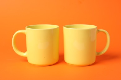 Photo of Two yellow ceramic mugs on orange background