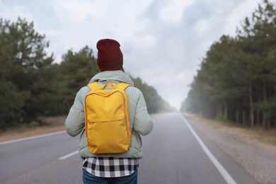 Woman with backpack on road near forest, back view