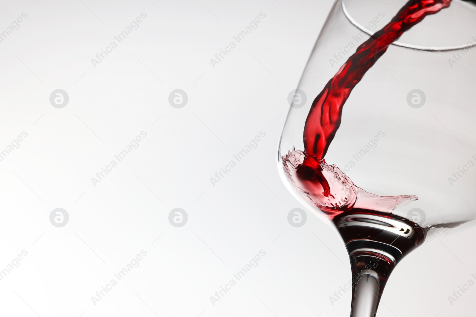 Photo of Pouring tasty red wine in glass on white background, closeup. Space for text