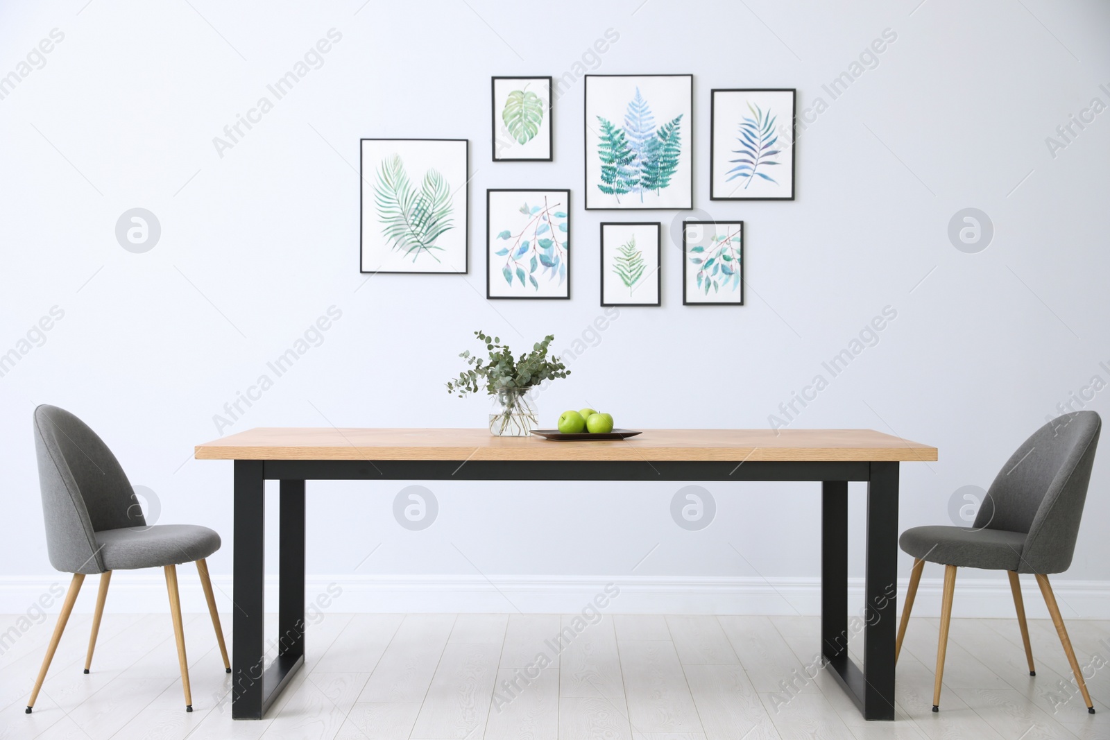 Photo of Stylish room interior with modern table, chairs and paintings of tropical leaves. Idea for design