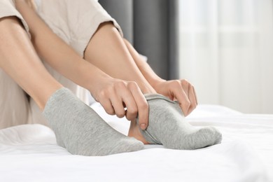 Woman putting on grey socks in bedroom, closeup