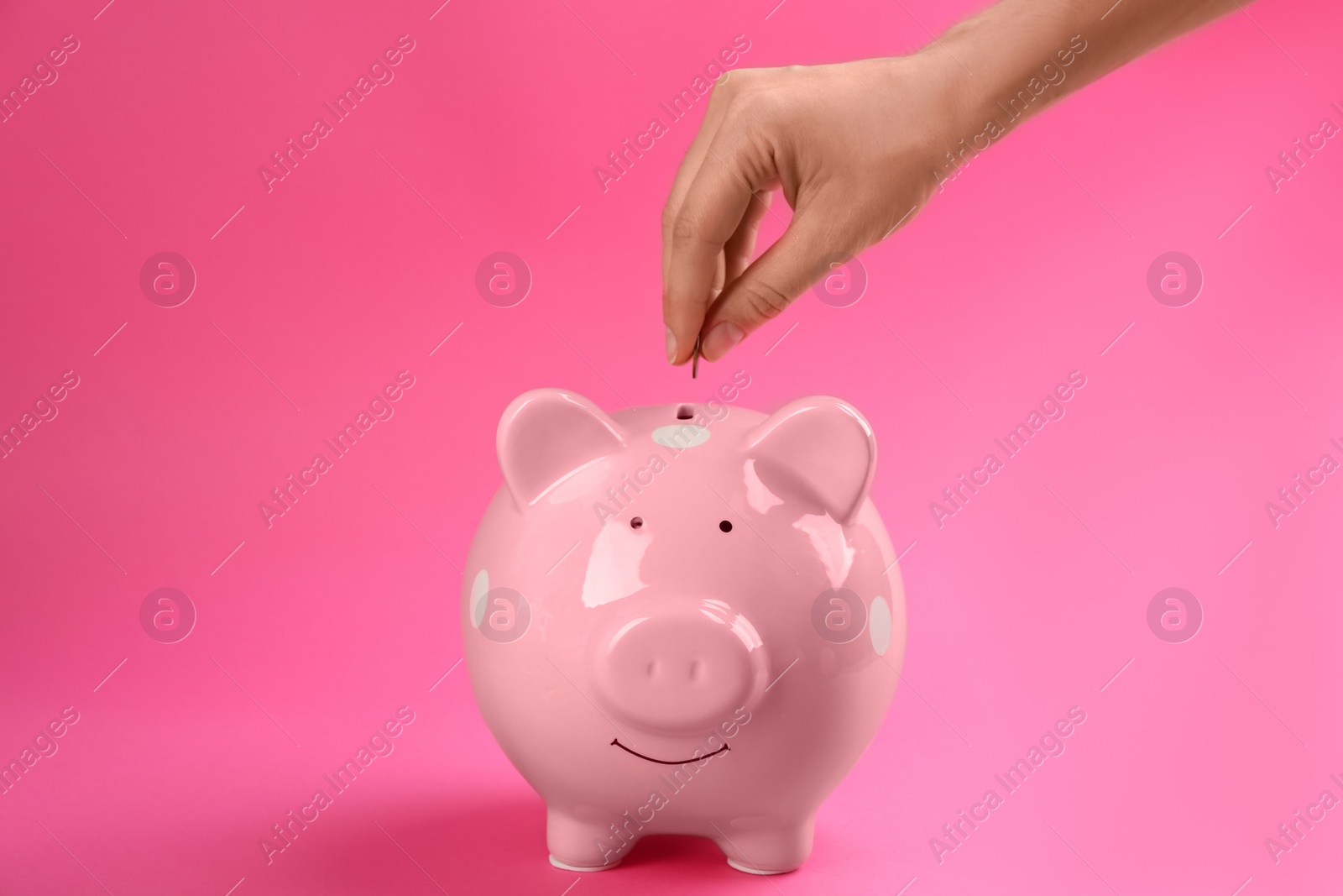 Photo of Woman putting coin into piggy bank on pink background, closeup