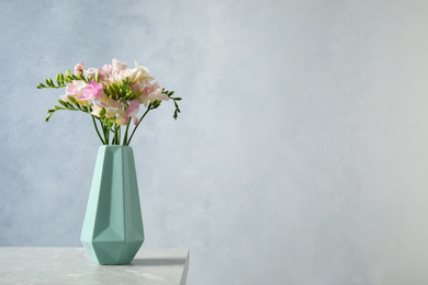 Beautiful blooming freesias in vase on table against blue background. Space for text