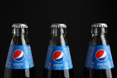 Photo of MYKOLAIV, UKRAINE - FEBRUARY 08, 2021: Glass bottles of Pepsi with water drops on black background, closeup