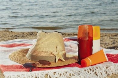 Sun protection products and beach accessories on blanket near sea, space for text