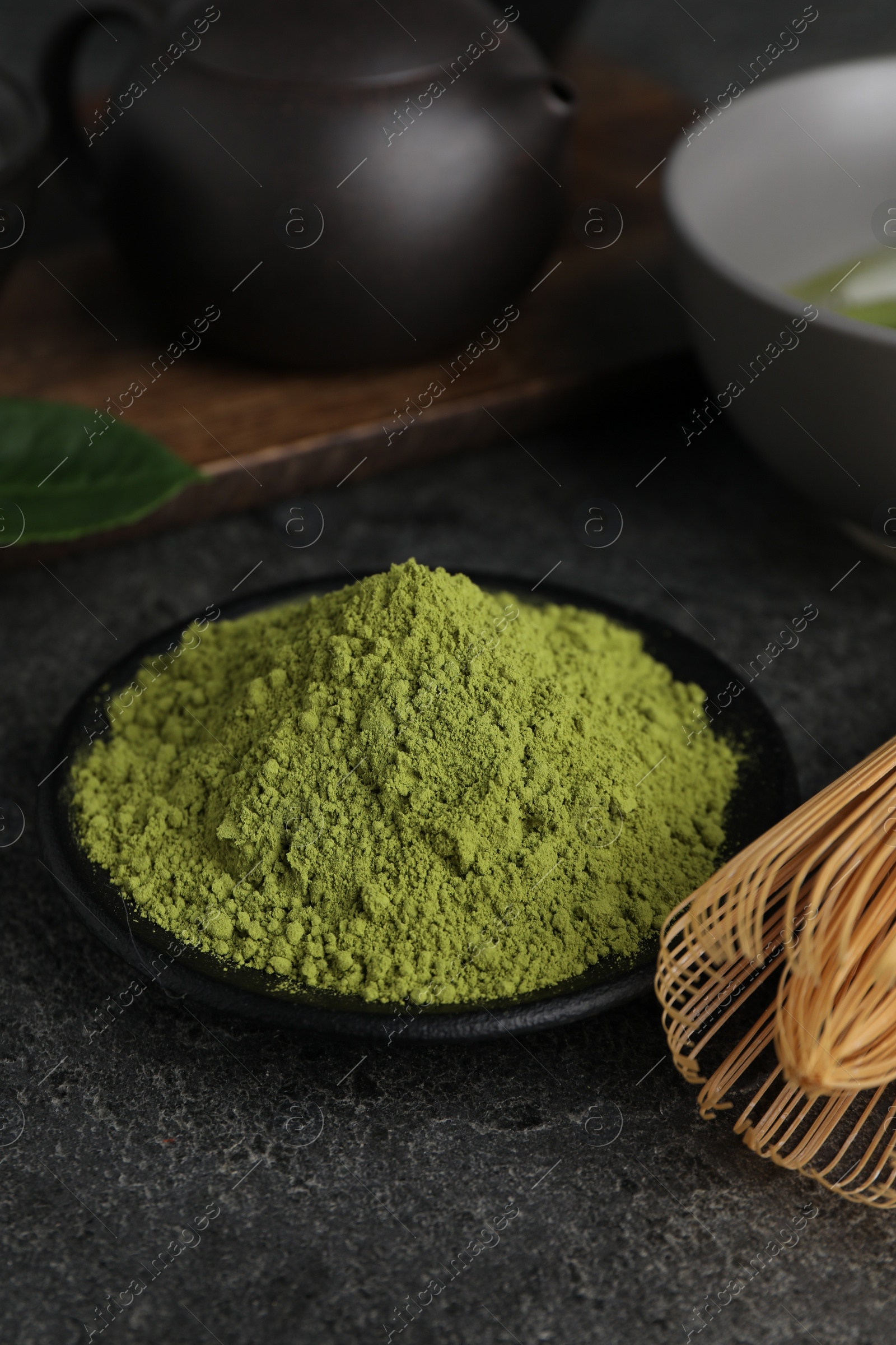 Photo of Green matcha powder and bamboo whisk on grey table, closeup. Space for text