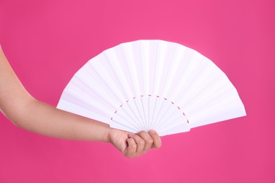 Photo of Woman holding white hand fan on pink background, closeup