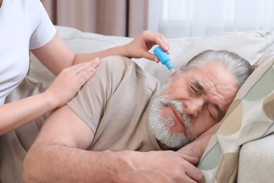 Photo of Young woman dripping medication into man's ear at home