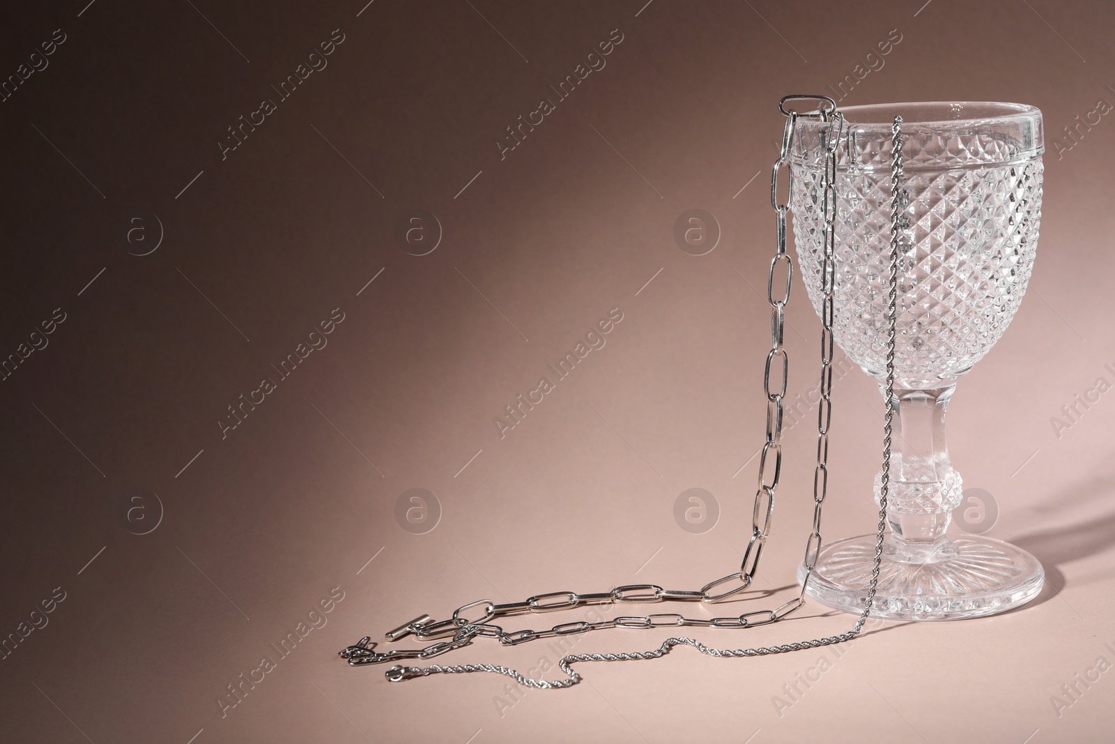 Photo of Different metal chains and glass on light brown background, space for text. Luxury jewelry