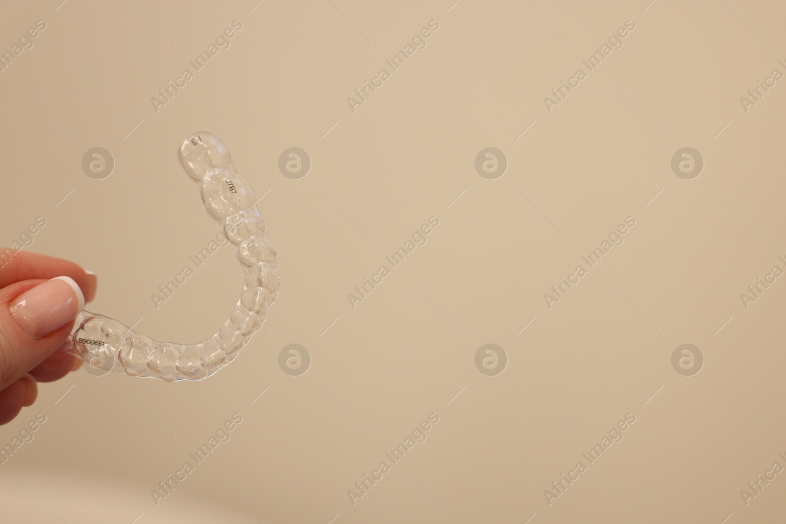 Photo of Woman with transparent dental aligner on beige background, closeup. Space for text