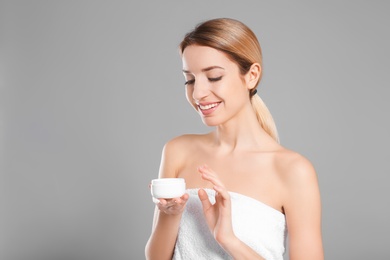 Young woman with jar of body cream on color background