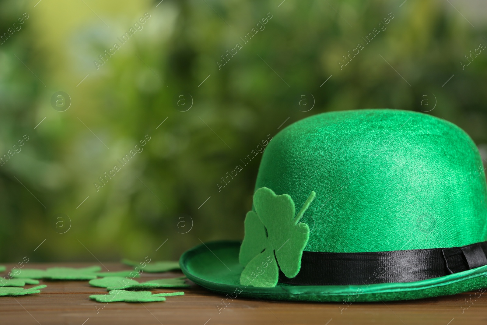 Photo of Leprechaun hat and clover leaves on wooden table against blurred background, space for text. St Patrick's Day celebration