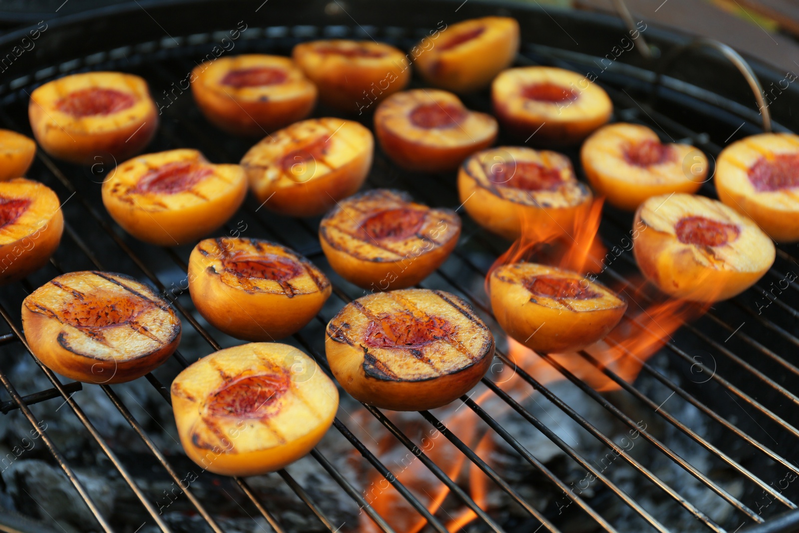 Photo of Modern grill with tasty cut peaches and flame, closeup