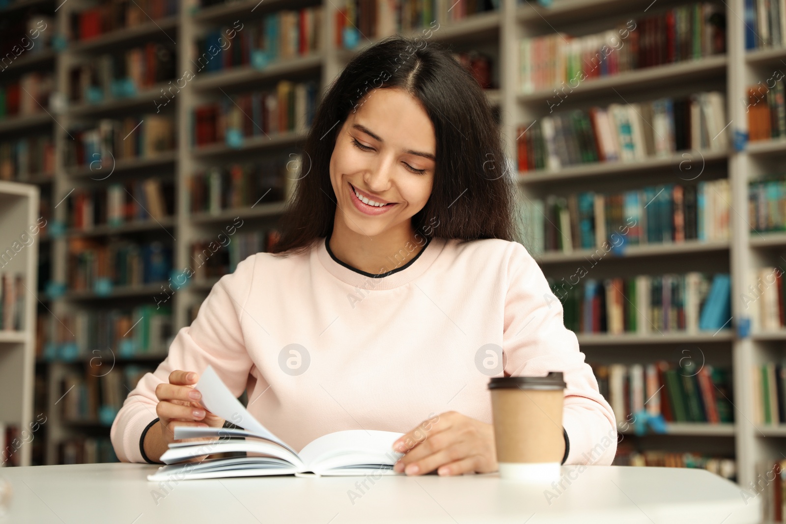 Photo of Young woman reading book at table in library