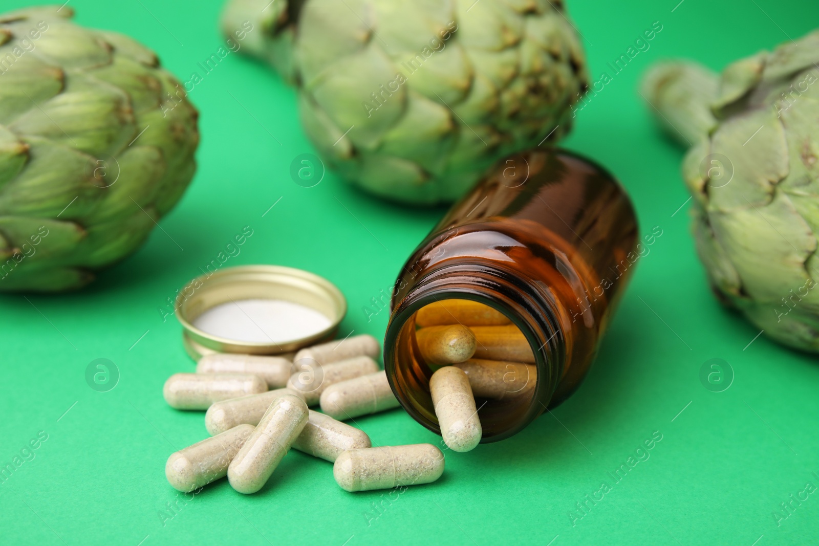 Photo of Bottle with pills and fresh artichokes on green background, closeup