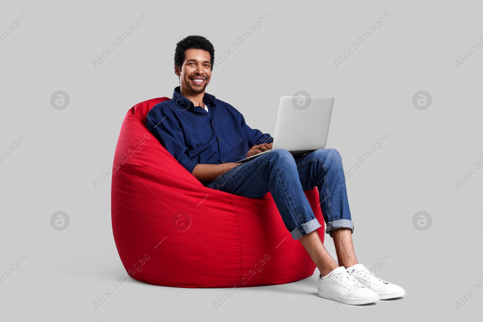 Photo of Happy man with laptop sitting on beanbag chair against grey background