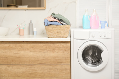 Photo of Wicker basket with laundry, detergents and washing machine in bathroom