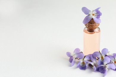 Photo of Beautiful wood violets and essential oil on white table, space for text. Spring flowers