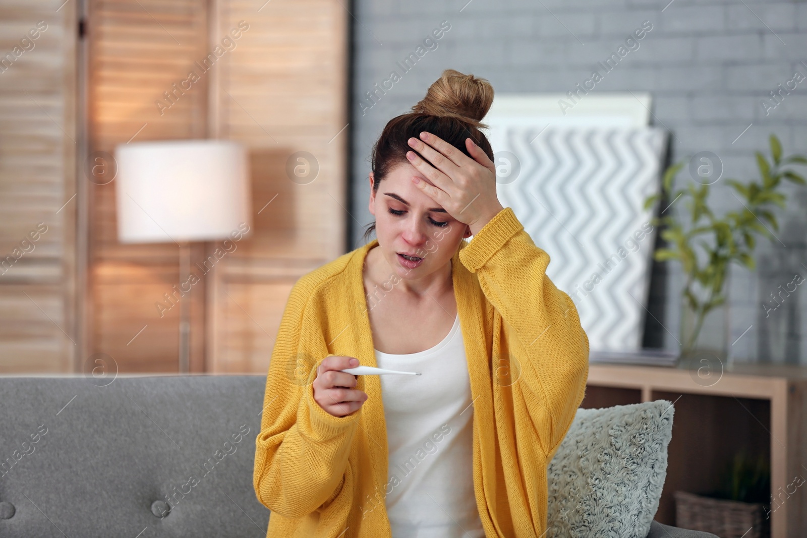 Photo of Sick woman with thermometer suffering from cold on sofa at home