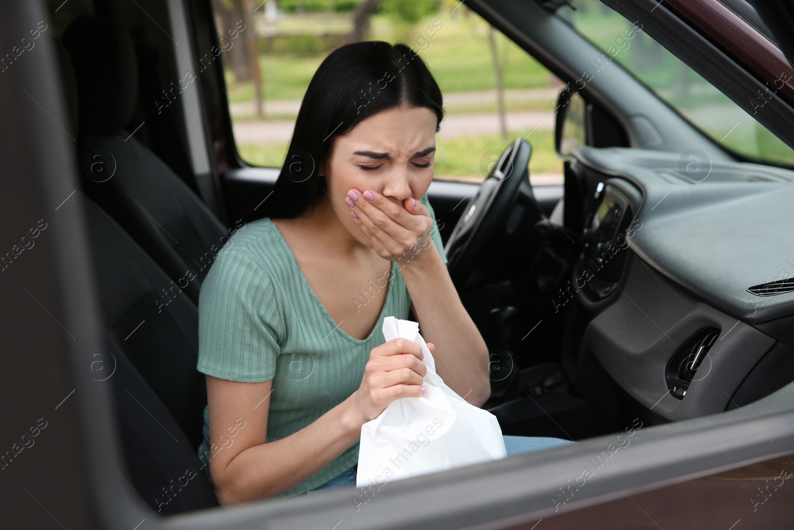 Photo of Young woman with paper bag suffering from nausea in car