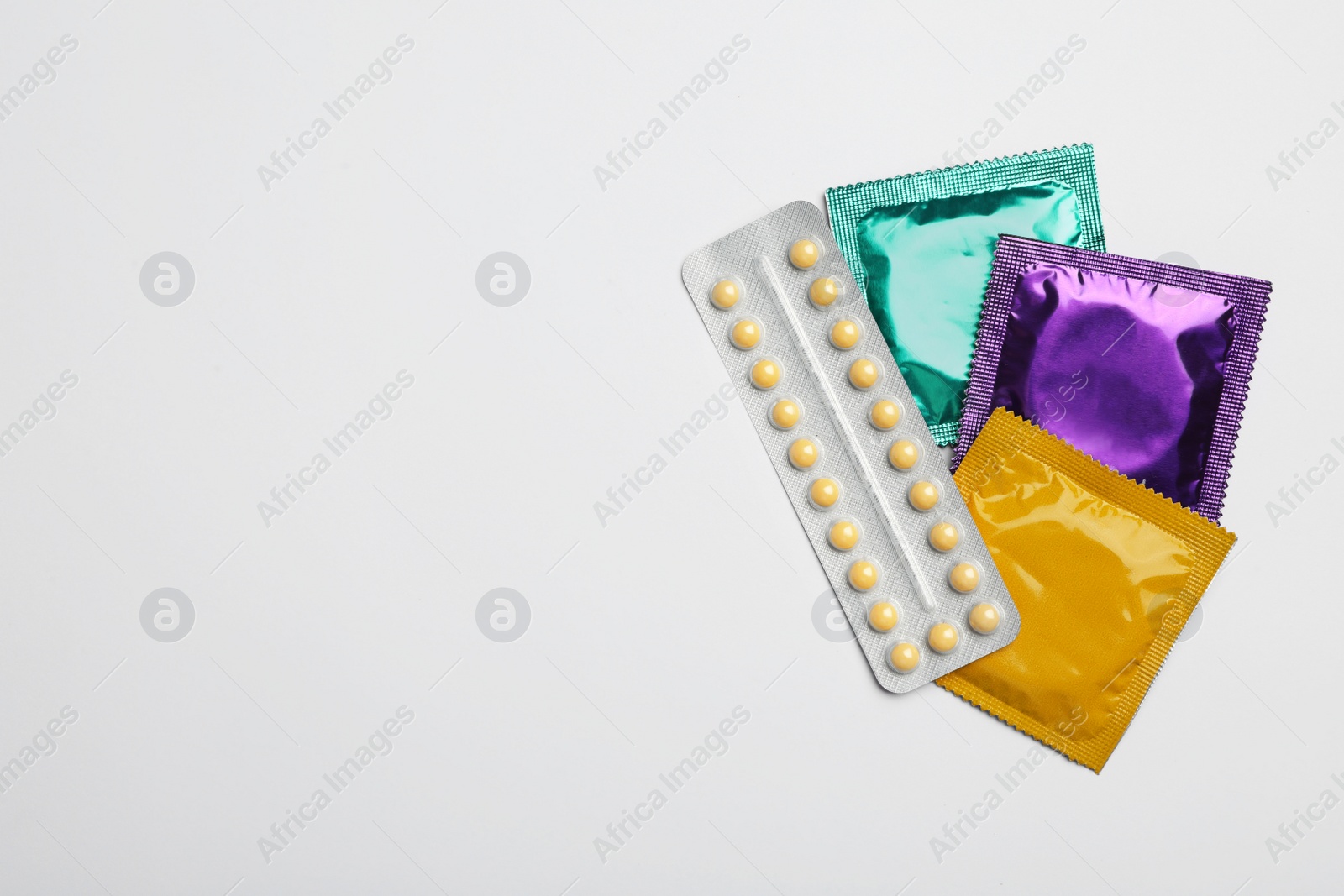 Photo of Condoms and birth control pills on light grey background, flat lay with space for text. Safe sex concept