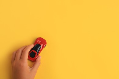 Photo of Child playing with toy car on yellow background, top view. Space for text
