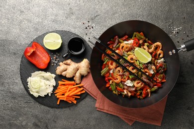 Photo of Shrimp stir fry with vegetables in wok and chopsticks on grey table, flat lay